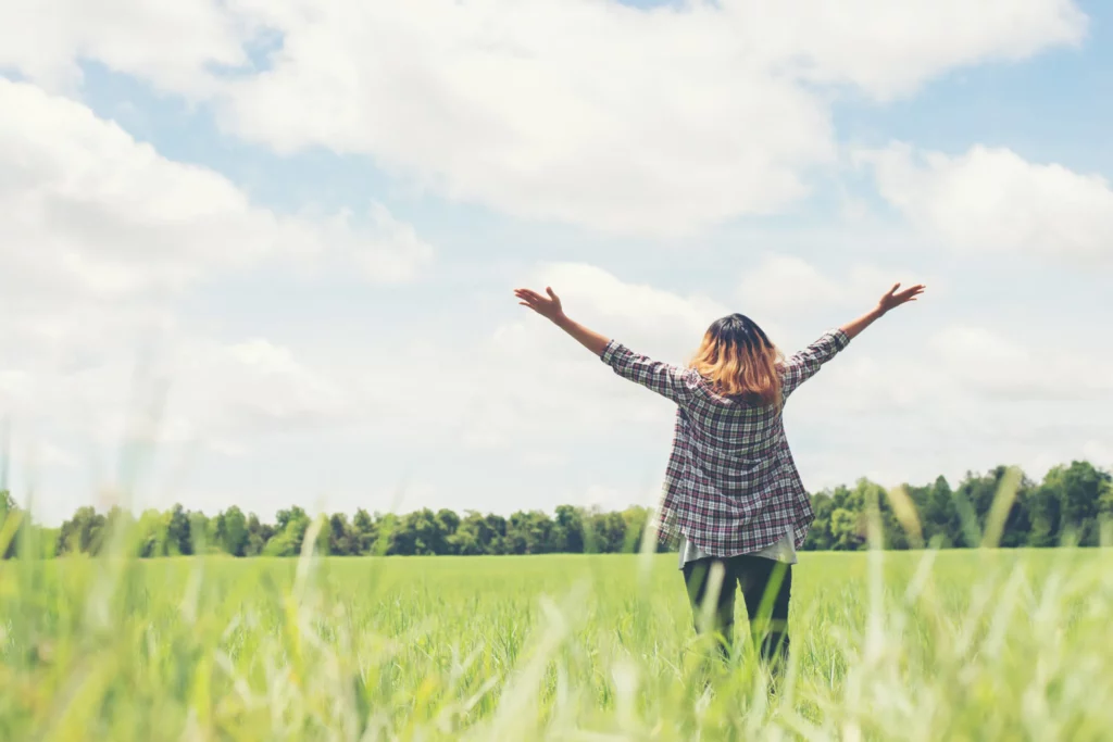 rear-view-of-young-woman-with-open-arms-in-the-meadow-scaled copie